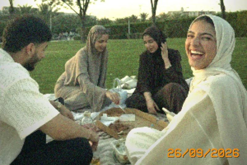 Friends laughing at a picnic in the park with an orange 26/09/2026 date stamp in the corner