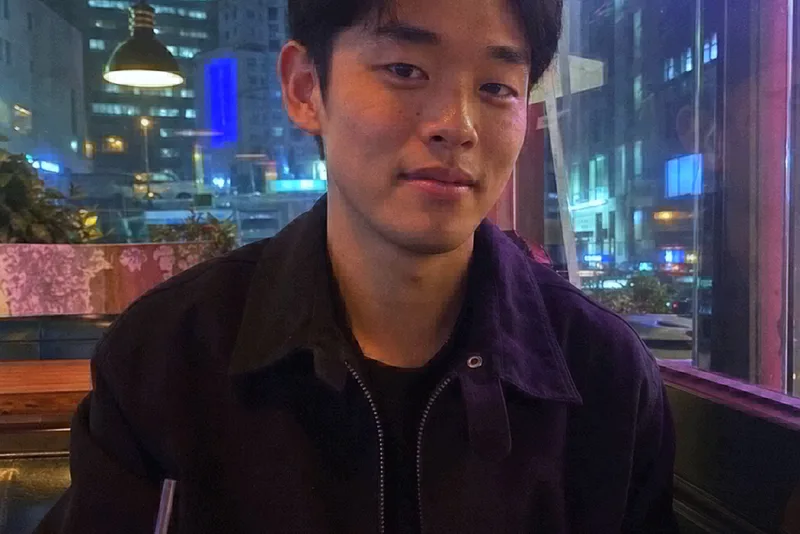 A young man in a diner booth at night, shot on Early Digital with cool flash and city lights behind